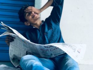 indian boy smiling and reading newspaper