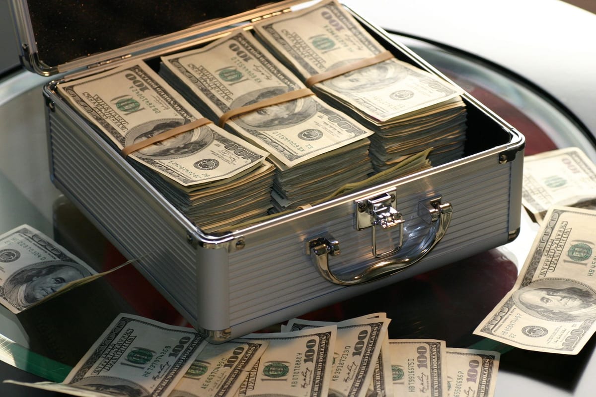 An open silver briefcase packed with banded stacks of hundred-dollar bills representing dry powder cash reserves.