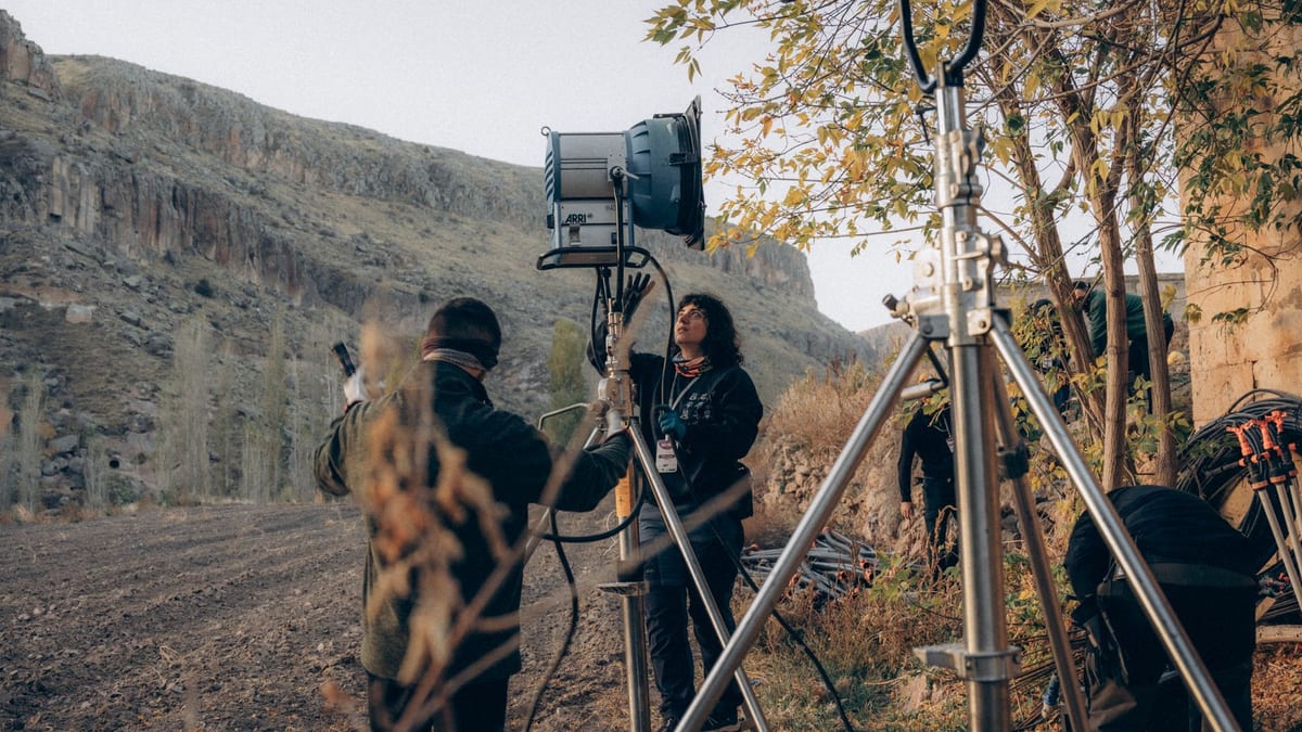 Film crew members adjust a large production light on a stand outdoors during a documentary shoot.