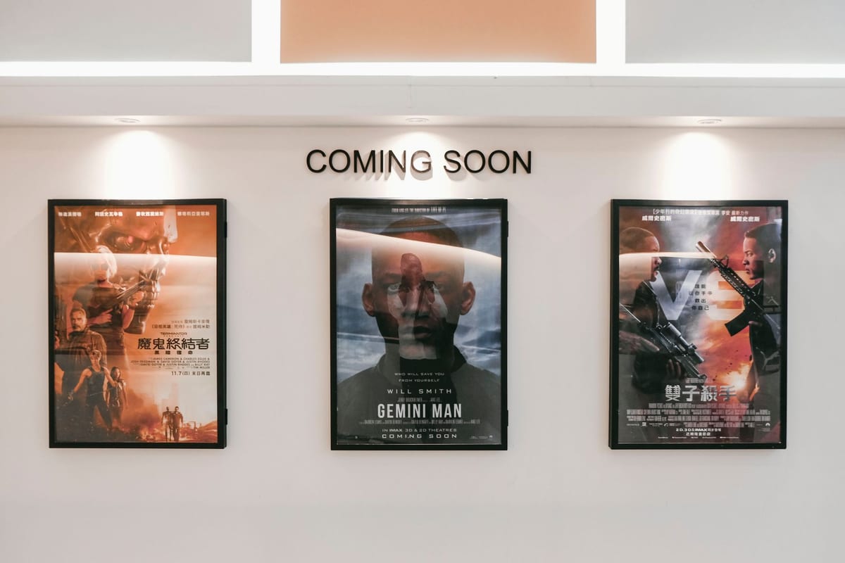 Three framed movie posters hang beneath a coming soon sign on a white wall in a cinema lobby.