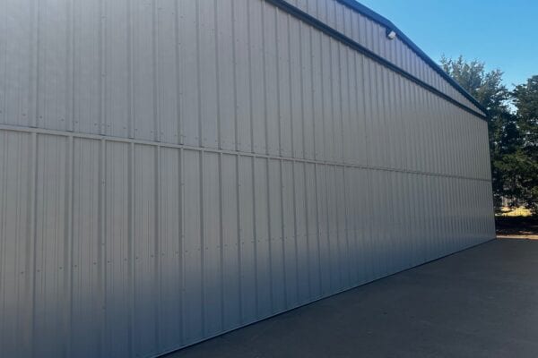 Exterior corrugated metal siding of a large steel aircraft hangar beside a concrete tarmac.